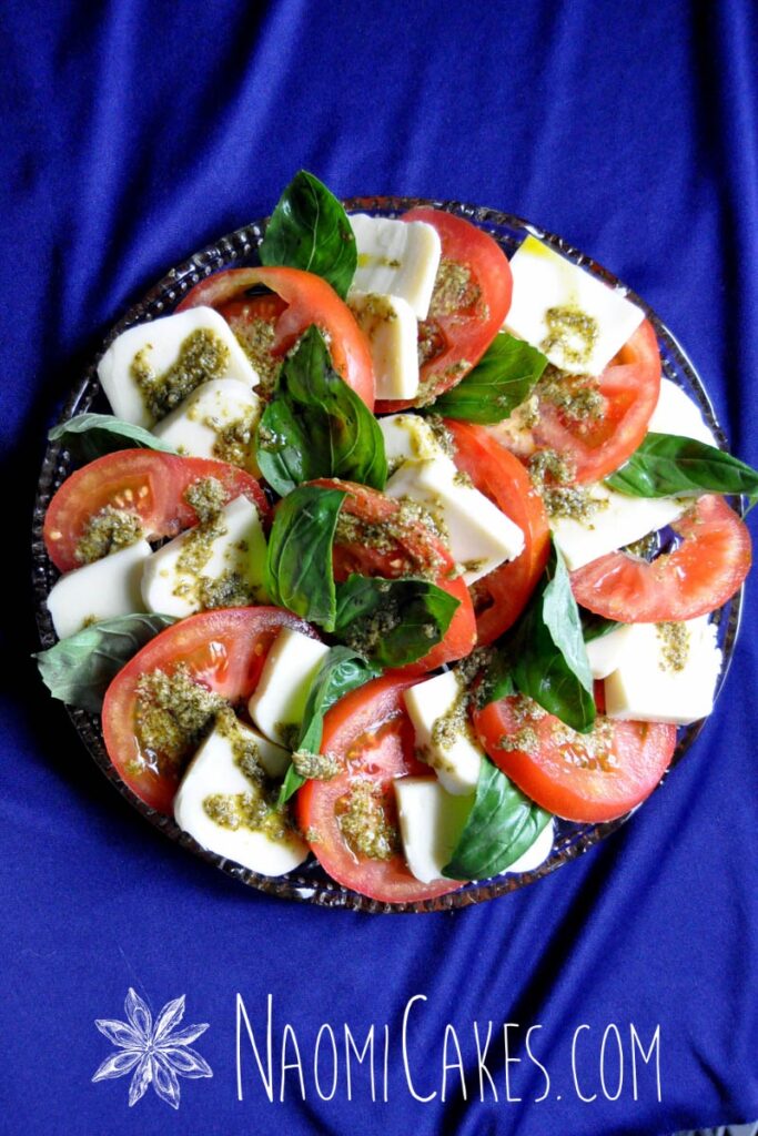 A spiral arranged Caprese salad on a round platter with a blue tablecloth background