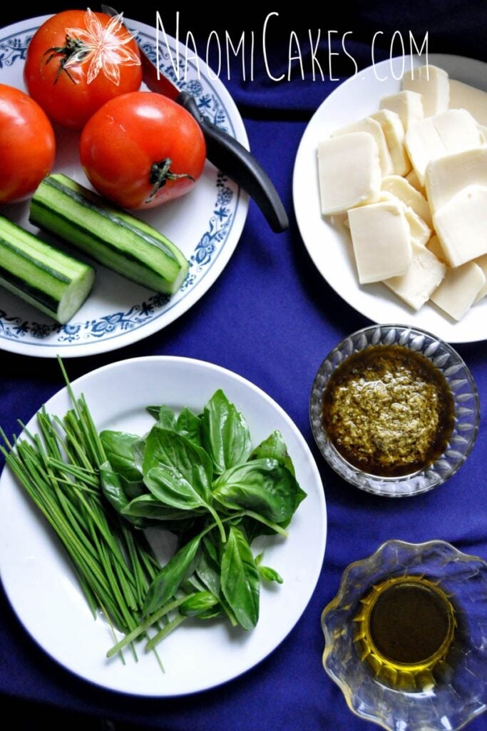 Caprese salad ingredients on a blue tablecloth background with a small bowl of pesto