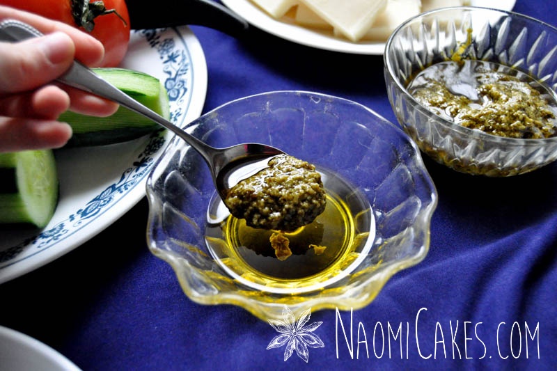 a teaspoon with pesto and olive oil with vegetables in the background