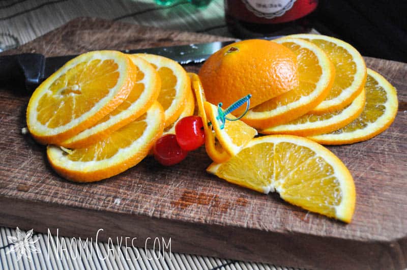 thinly sliced oranges and maraschino cherries on a cutting board