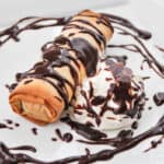 baked baked mars bar in phyllo pastry on a plate with chocolate sauce drizzled in a circle around it and cream on the side