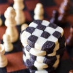 stack of checkerboard cookies amid chess pieces on a checker board