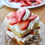 a square mini strawberry shortcake on a glass plate on a cutting board with strawberries in the background