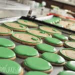 a cookie sheet lined with round cookies, some of which are filled with green royal icing