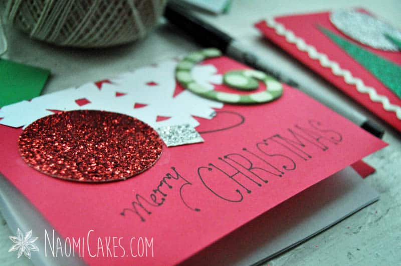 a red a close of up of homemade Christmas card with glitter ornaments and paper cutouts