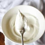 overhead view of a spoonful of royal icing over a bowl sitting on a table with a white cloth underneath it