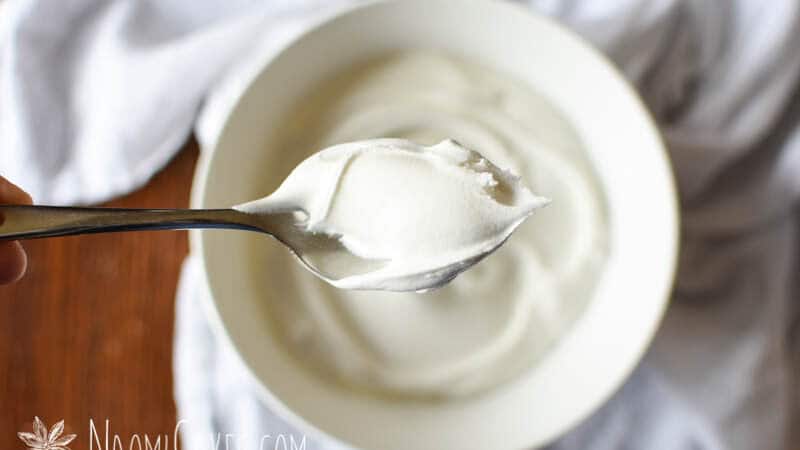 overhead view of a spoonful of royal icing over a bowl sitting on a table with a white cloth