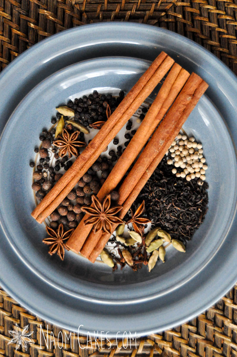 vertical image of star anise, cinnamon sticks and other whole chai spices and black tea on two blue plates