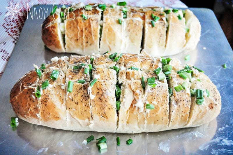 2 loaves of bread stuffed with garlic butter and green onions ready to go in the oven