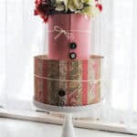 2 tiers of foam cake dummies wrapped in pink and floral scrapbooking paper, topped with silk hydrangias, fastened with button thumb tacks, and tied with string