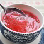 spoon dipped into pink rhubarb sauce in a wide mouth tea cup on patterned paper background