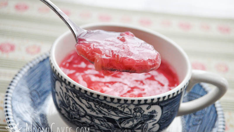 spoon showing pink rhubarb sauce in a tea cup on patterned paper background