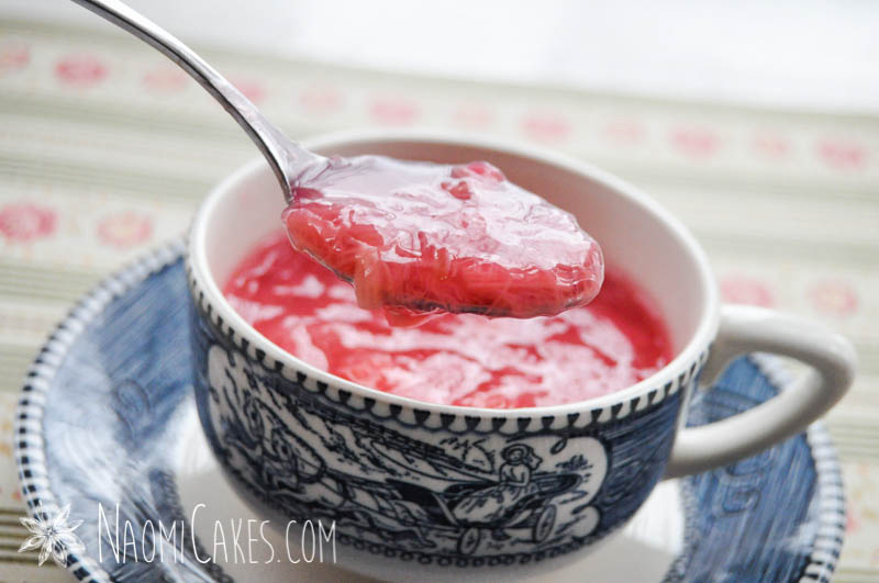 spoon showing pink rhubarb sauce in a tea cup on patterned paper background