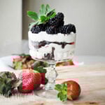 horizontal image of a mini cheesecake trifle with blackberries and strawberries on a wooden board with fresh strawberries beside