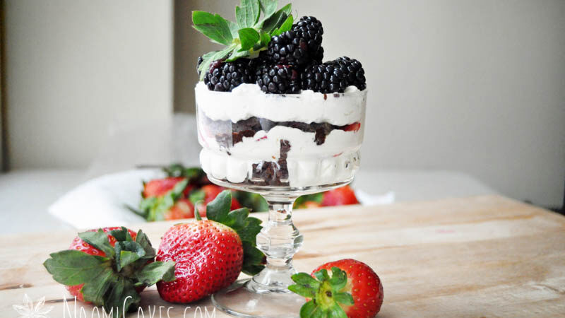 horizontal image of a mini cheesecake trifle with blackberries and strawberries on a wooden board with fresh strawberries beside