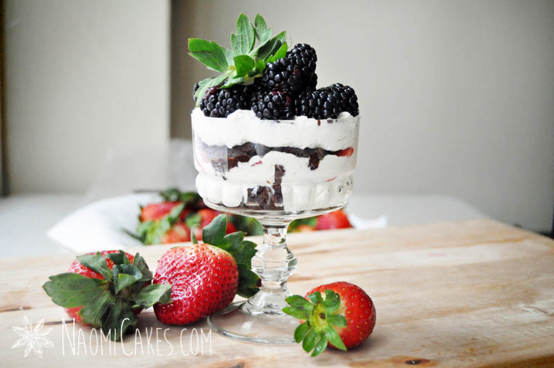 horizontal image of a mini cheesecake trifle with blackberries and strawberries on a wooden board with fresh strawberries beside