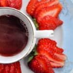 china cup of hot punch with strawberries around it on a blue plate close up
