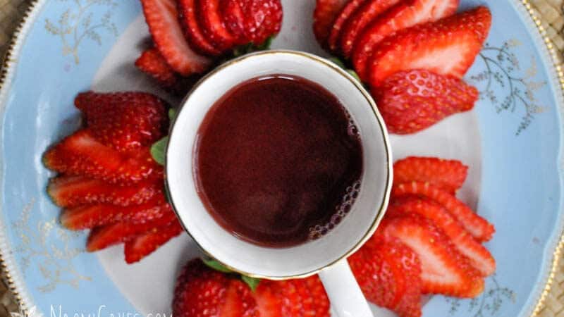 china cup of hot punch with strawberries around it on a blue plate close up overhead view
