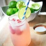 a mason jar with raspberry limeade, a wedge of lime and a blue striped paper straw