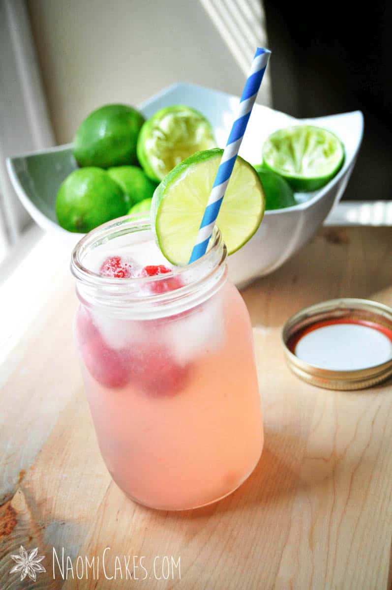 a mason jar with raspberry limeade, a wedge of lime and a blue striped paper straw