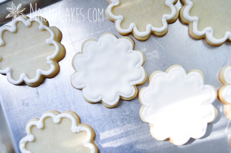 flower shaped sugar cookies in the process of being decorated with white frosting