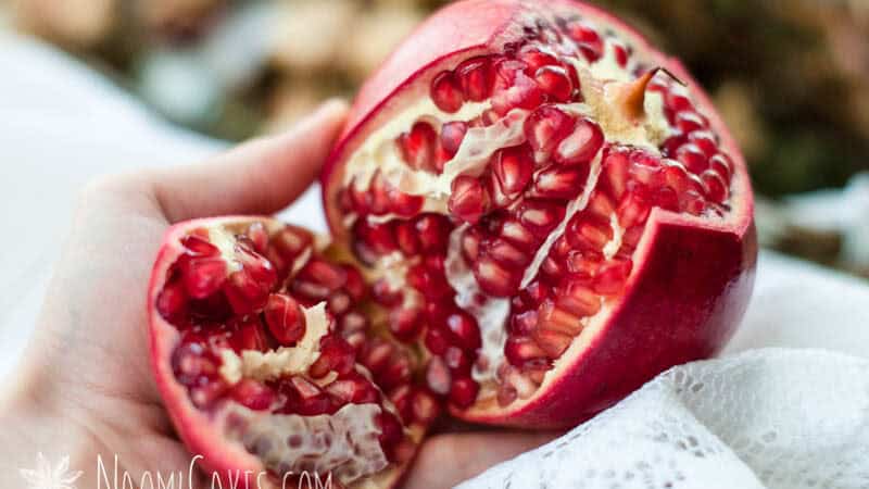 hand holding a cut open pomegranate with the seeds exposed