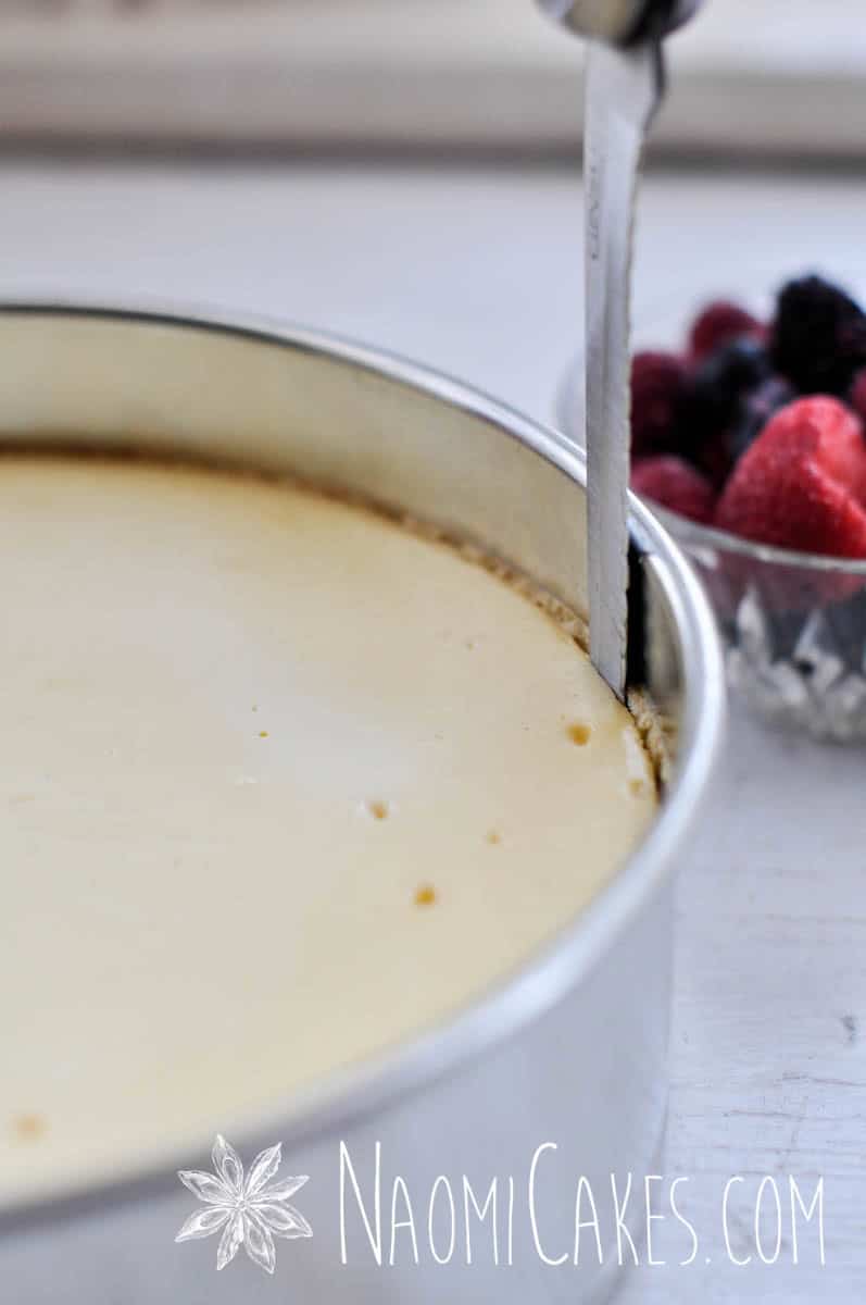 knife cutting along the edge of a baked cheesecake to release it from the pan