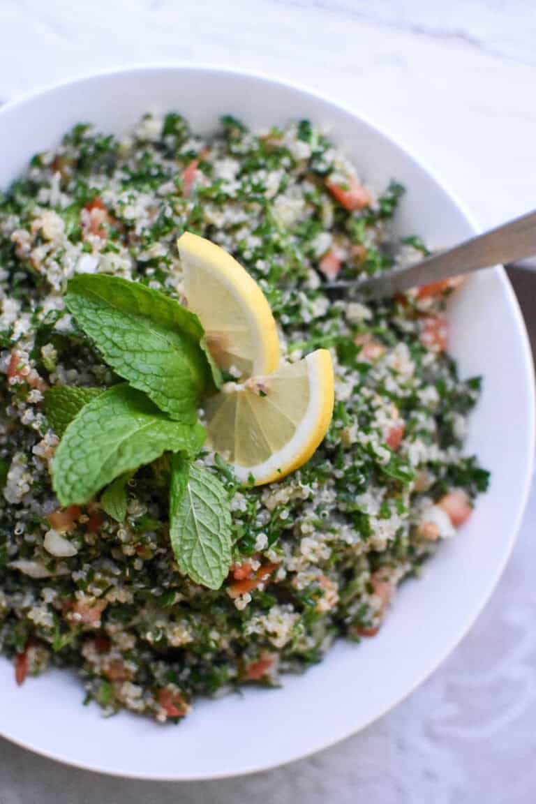 an overhead view of a bowl of quinoa tabbouleh with lemon and fresh mint on top on a white background