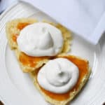 overhead view of a scone with jam and cream on a white plate