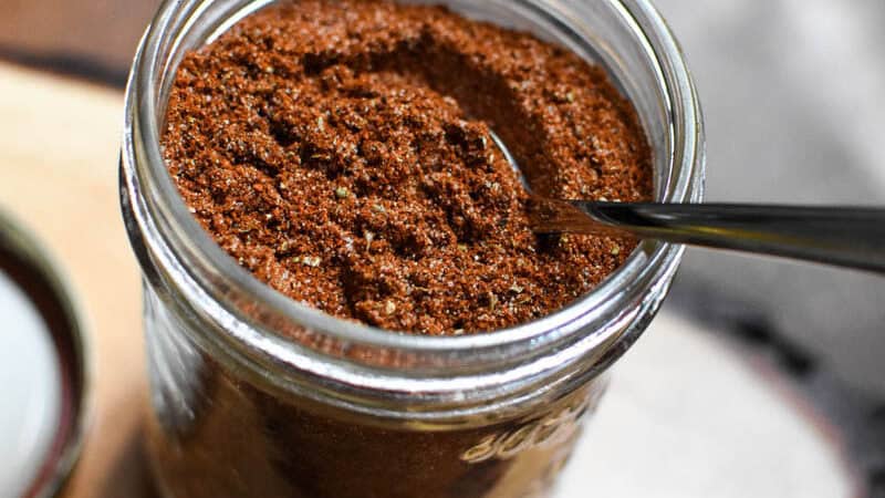a mason jar with homemade taco seasoning on a wooden board with a spoon in it