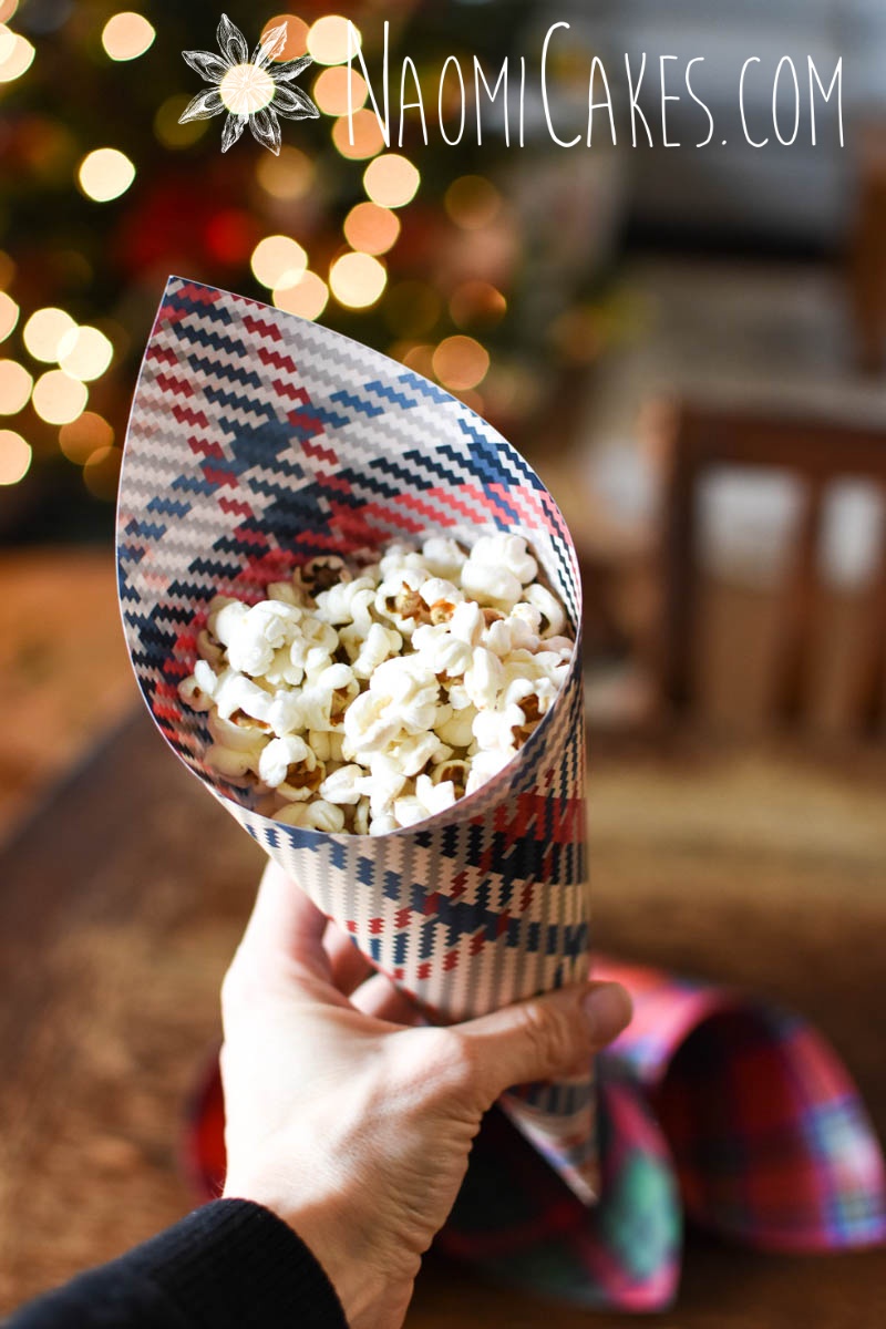 Blue and red on white plaid Christmas paper cone with popcorn in front of a Christmas tree