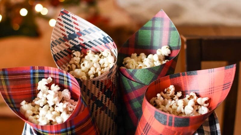 plaid Christmas paper cones filled with popcorn in front of Christmas lights