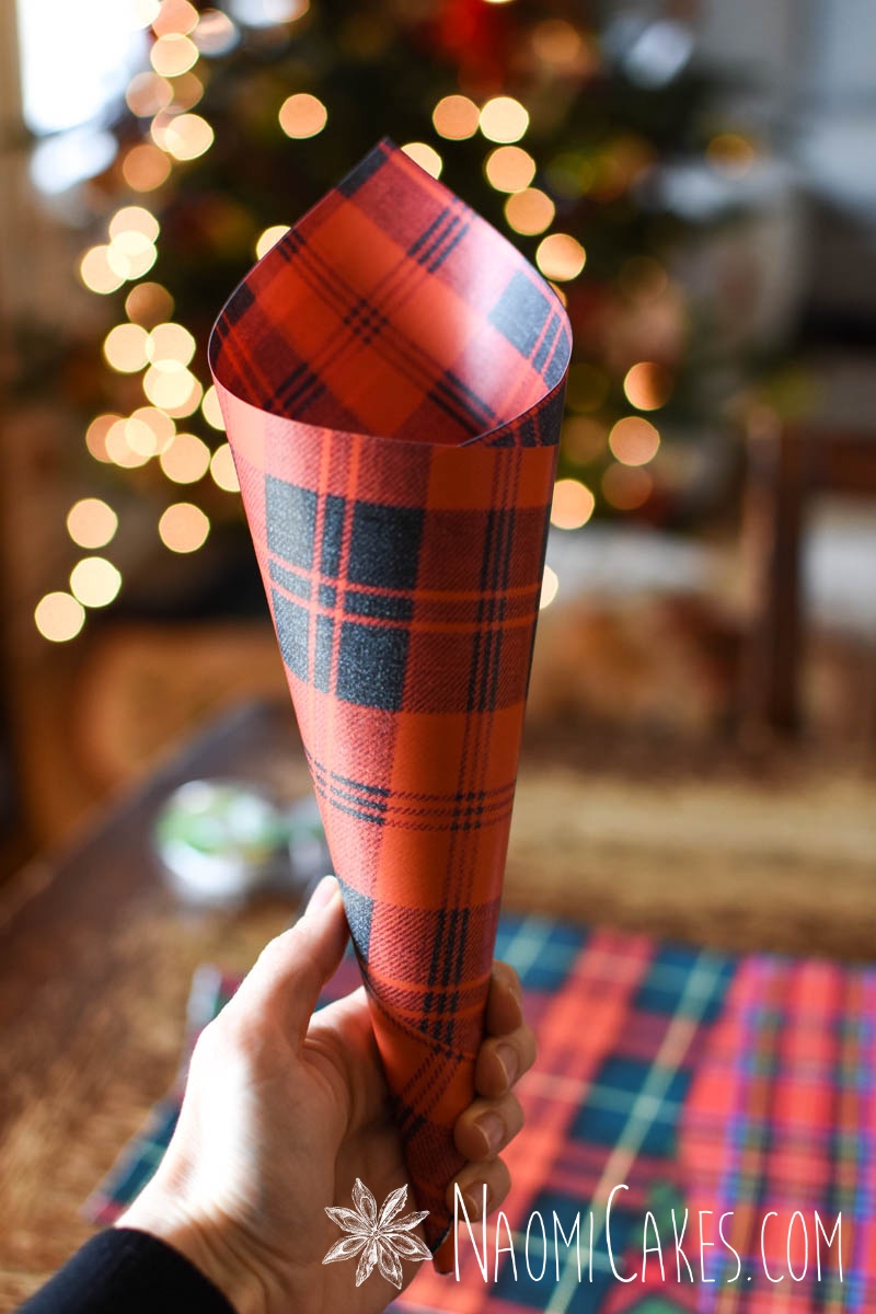 Hand holding a red plaid Christmas paper cone in front of Christmas lights
