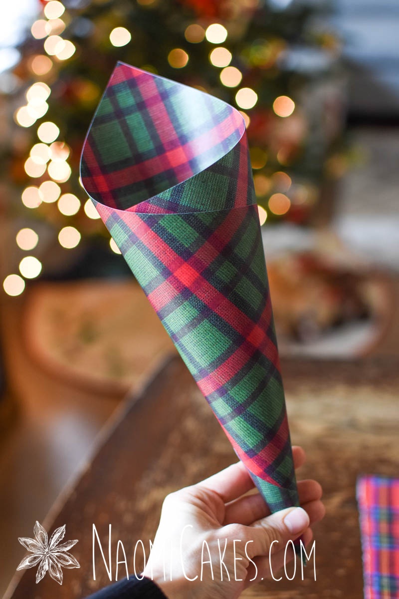 hand holding green plaid Christmas paper cone in front of Christmas tree