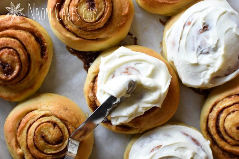 Some unfrosted and some frosted cinnamon rolls on a pan, with a knife spreading icing on one