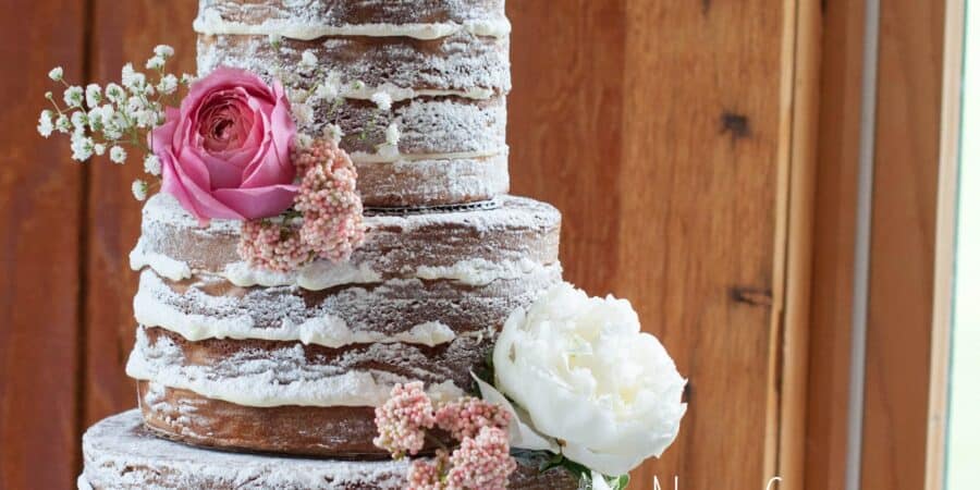 close up image of a 3 tier naked cake wedding cake with pink flowers and wooden background