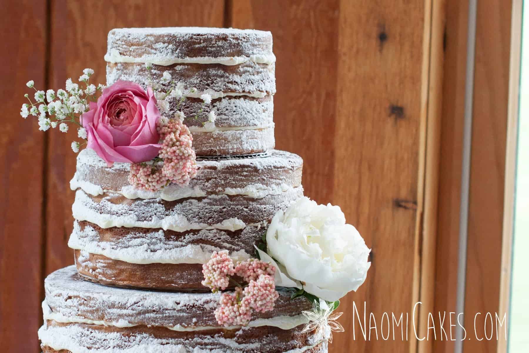 close up image of a 3 tier naked cake wedding cake with pink flowers and wooden background