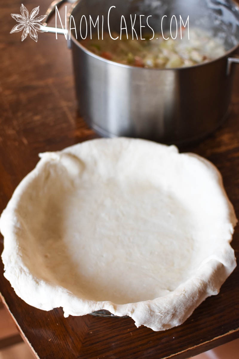 pie plate lined with pastry with a pot of meat pie filling in the background