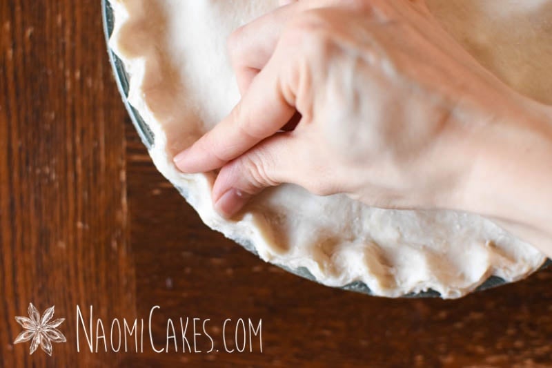 a hand fluting the edges of a pie on a wooden table
