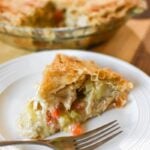 close up picture of a slice of chicken pie with the whole pie behind it and a fork on a white plate