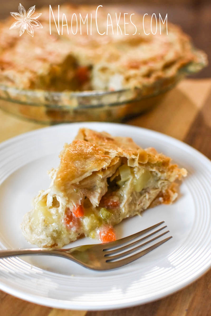 close up picture of a slice of chicken pie with the whole pie behind it and a fork on a white plate