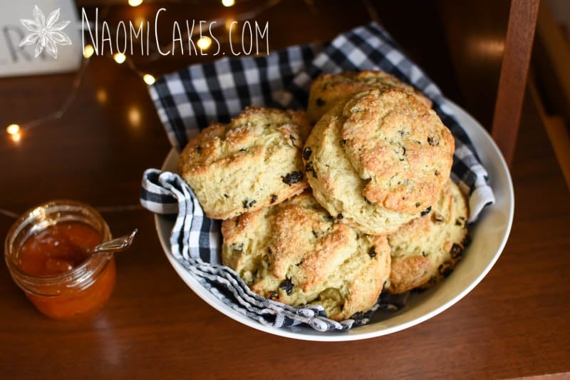 bowl of large round currant scones on a wooden cabinet with fairy lights, black and white checkered cloth and home decor sign