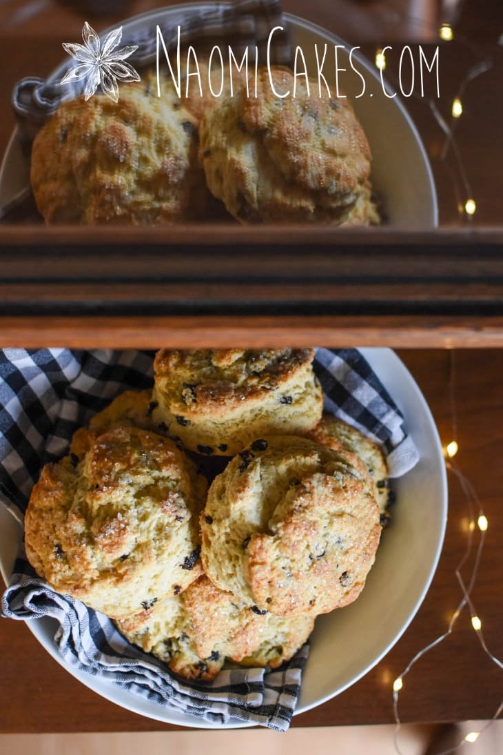 bowl of currant scones reflecting in a glass display case with a checkered tea towel and fairy lights