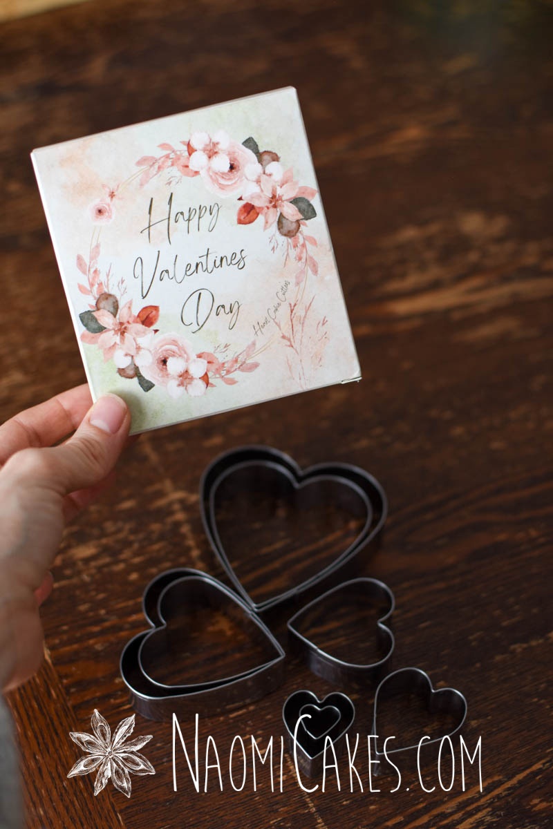 heart shaped cookie cutter set and a hand holding a box that says Happy Valentines Day over a wooden table