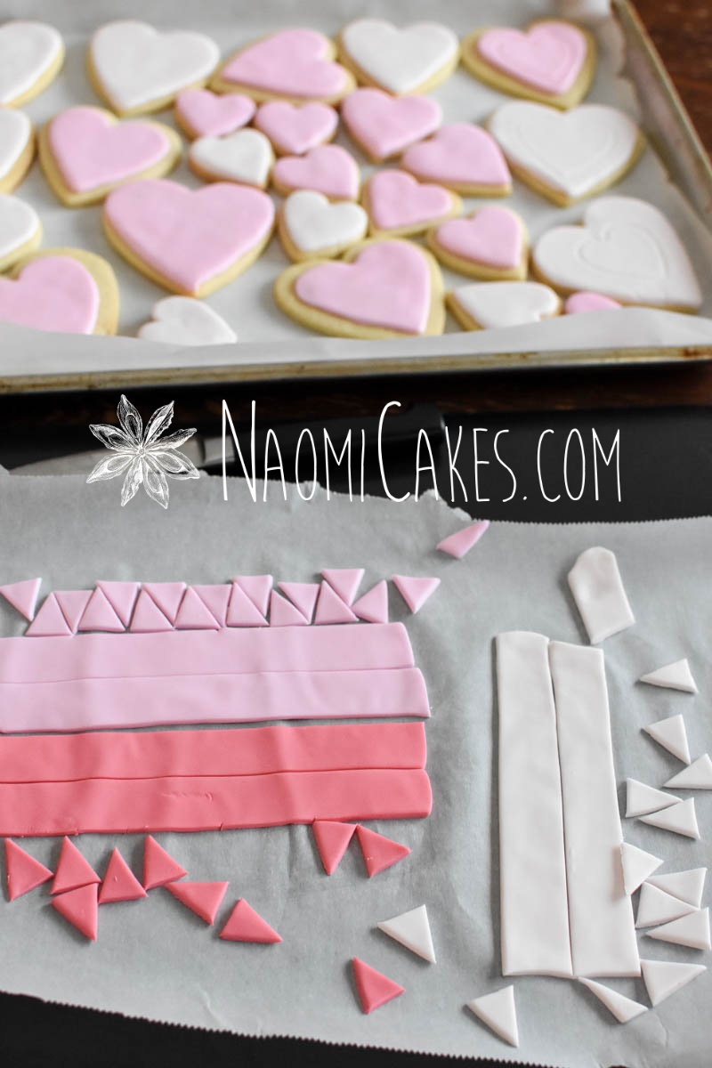 Strips of pink fondant in various shades cut into triangles with pink and white heart cookies in the background