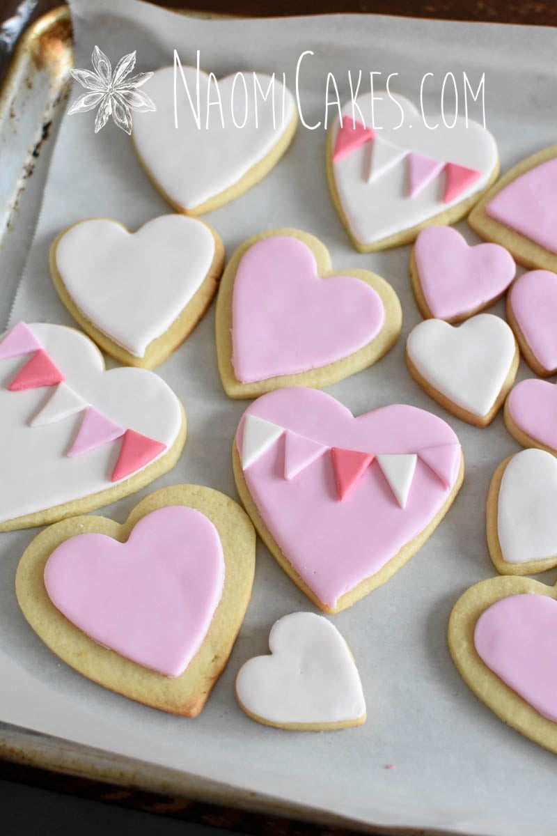 in process picture of heart cookies in pink and white being decorated for Valentines Day on white parchment paper