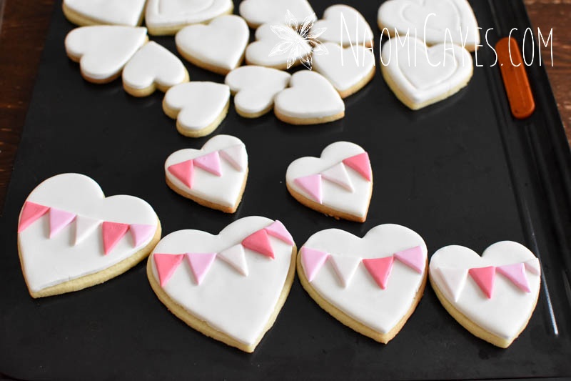 in process picture of heart cookies in pink and white being decorated for Valentines Day on a black pan
