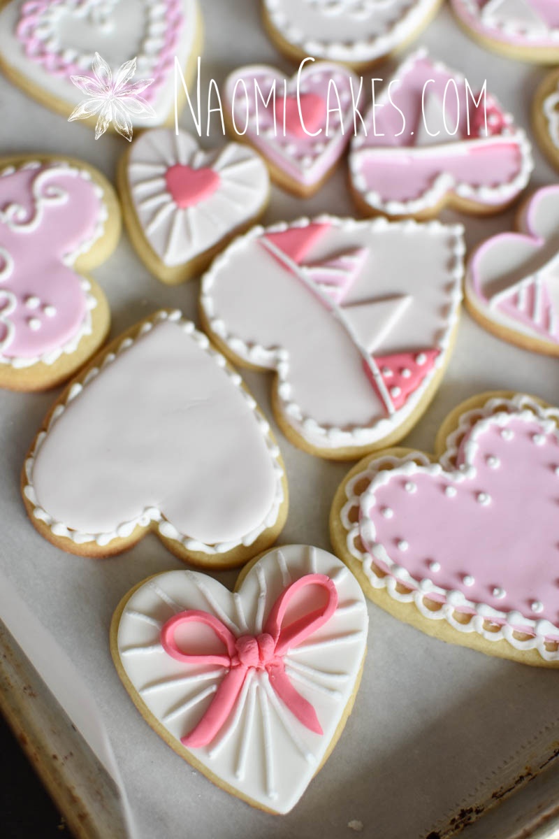 heart cookie with a pink bow and other assorted valentine cookies in pink and white