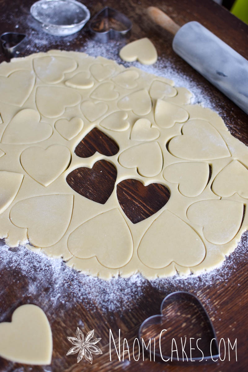 sugar cookie dough being cut with a heart cutter on a wooden table