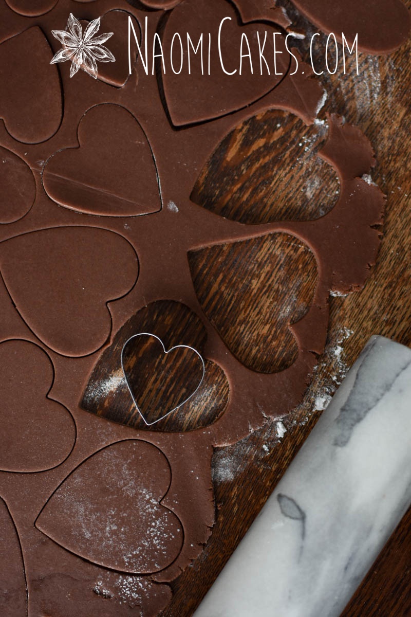 chocolate sugar cookie dough being cut with a heart cutter on a wooden table
